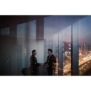 Umělecká fotografie Businessmen shaking hands in office at night, Shannon Fagan, (40 x 26.7 cm)